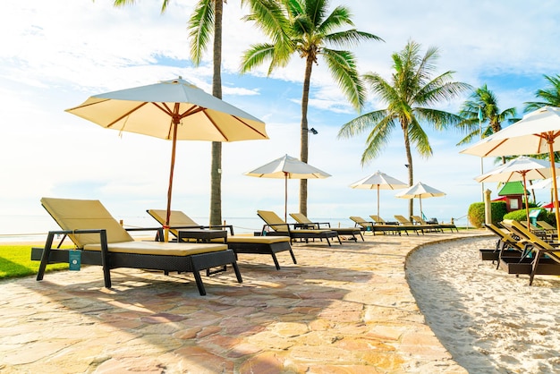 Beautiful luxury umbrella and chair around outdoor swimming pool in hotel and resort with coconut palm tree on sunset  or sunrise sky - holiday and vacation concept