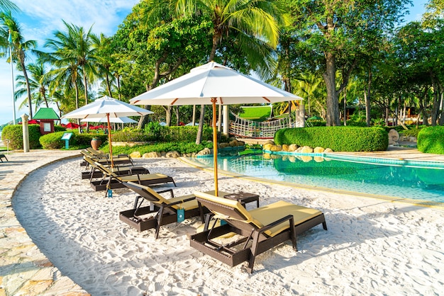 Bellissimo ombrellone e sedia di lusso intorno alla piscina all'aperto in hotel e resort con palme da cocco sul cielo al tramonto o all'alba