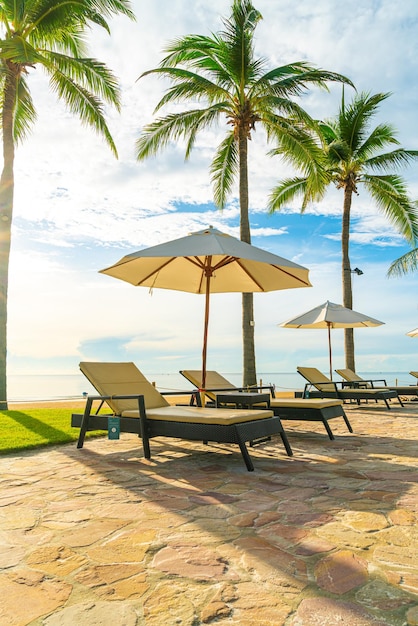 Beautiful luxury umbrella and chair around outdoor swimming pool in hotel and resort with coconut palm tree on sunset or sunrise sky