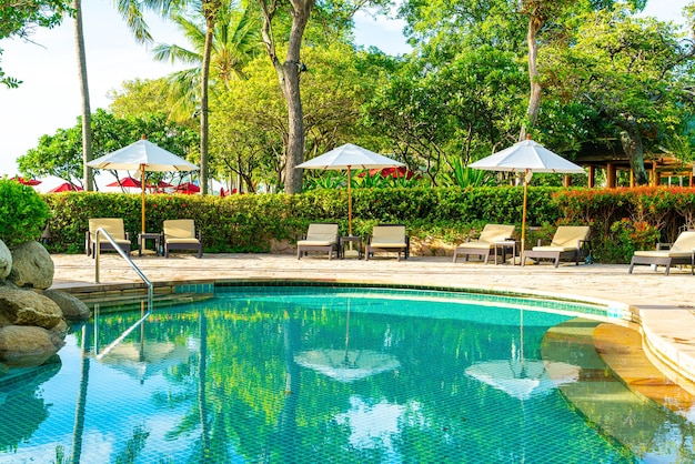 Bei ombrello e sedia di lusso intorno alla piscina all'aperto in hotel e località di soggiorno con l'albero del cocco sul cielo di alba o di tramonto