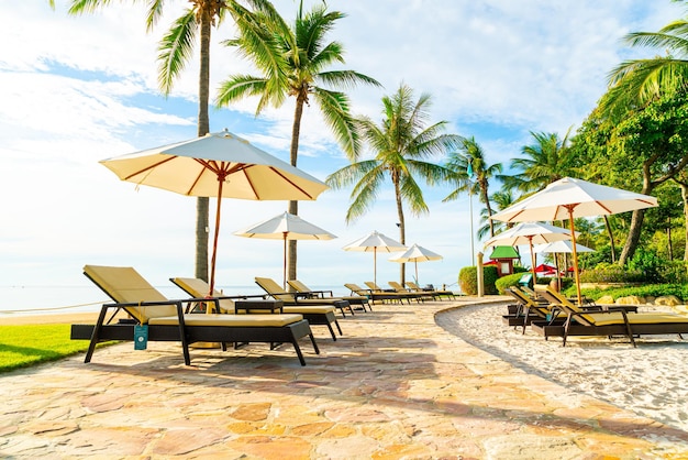 Beautiful luxury umbrella and chair around outdoor swimming pool in hotel and resort with coconut palm tree on sunset or sunrise sky