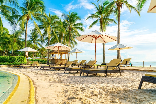 Beautiful luxury umbrella and chair around outdoor swimming pool in hotel and resort with coconut palm tree on sunset or sunrise sky