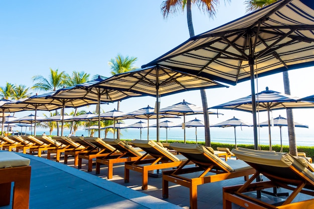 Beautiful luxury umbrella and chair around outdoor swimming pool in hotel and resort with coconut palm tree