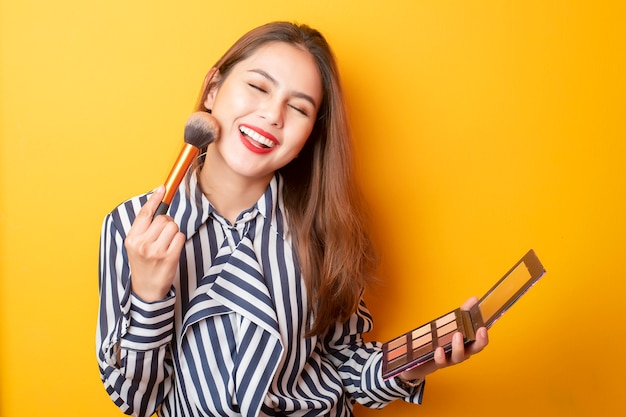 Beautiful makeup artist woman is happy on yellow background 