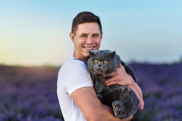 Bellissimo uomo con un gatto britannico nel campo di lavanda al tramonto. fantastica atmosfera estiva.