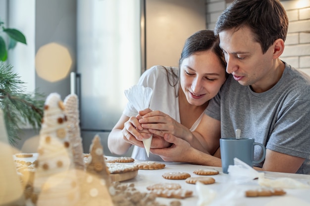 Beautiful man and woman decorate christmas gingerbread two people draw a heart on the cookie stylish...