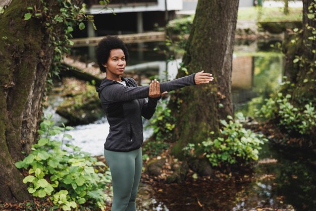 Beautiful mature African American female runner stretching before jogging in nature.