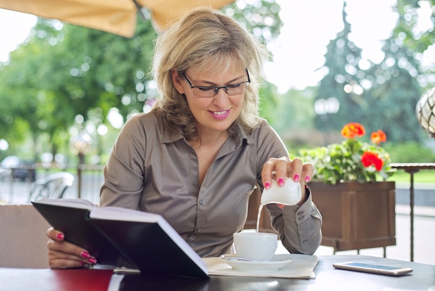 Beautiful mature business woman drinking coffee at break in outdoor restaurant