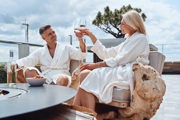 Photo beautiful mature couple in bathrobes enjoying fruits and wine while relaxing in luxury hotel outdoors