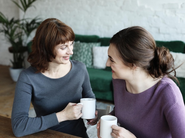 Beautiful mature mother and her adult daughter are drinking coffee