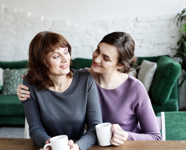 Beautiful mature mother and her adult daughter are drinking coffee