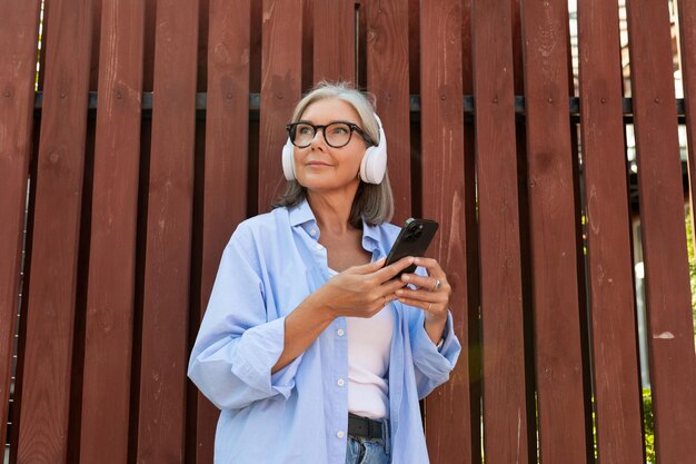 Photo beautiful mature old lady with gray hair dressed enjoys music in headphones on the street