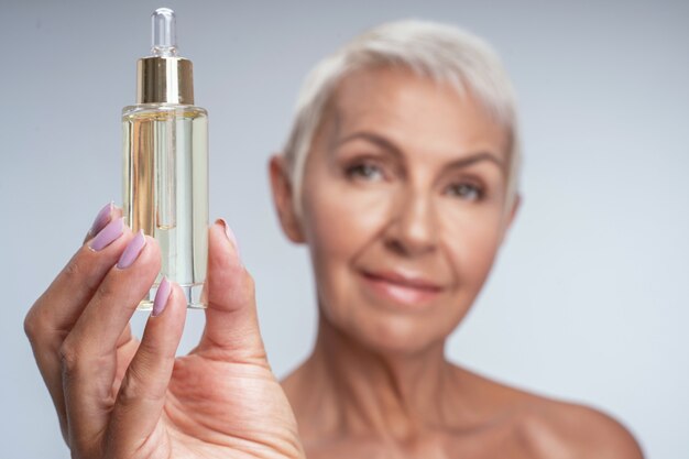 Beautiful mature woman holding face serum in her hand