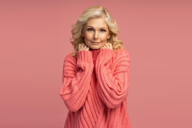 ピンクの背景に分離されたスタイリッシュな冬のセーターを着ている美しい成熟した女性