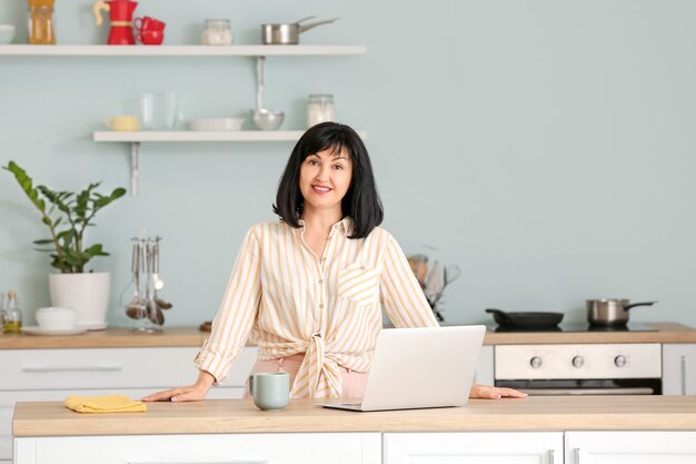 Bella donna matura con laptop in cucina