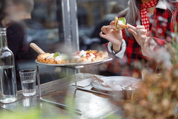 La bella donna asiatica matura sta mangiando la pizza nella terrazza del caffè