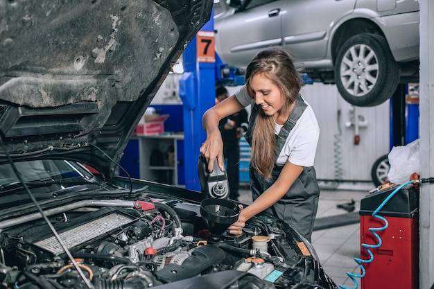 Foto la bella ragazza del meccanico in una tuta nera e una maglietta bianca cambia l'olio in un'auto nera. concetto di riparazione auto