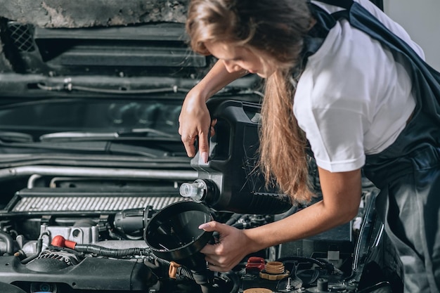 La bella ragazza del meccanico in una tuta nera e una maglietta bianca cambia l'olio in un'auto nera. foto ravvicinata. concetto di riparazione auto