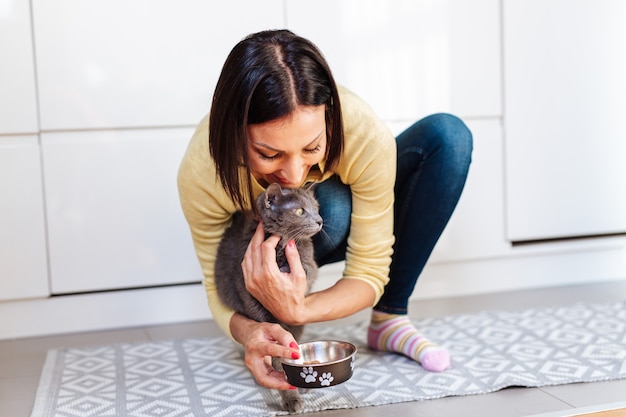 家で猫に餌をやる美しい中年女性。