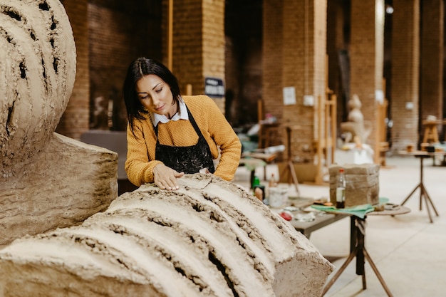 ゴージャスな彫刻に取り組んでいる美しい中年女性のプロの彫刻家。