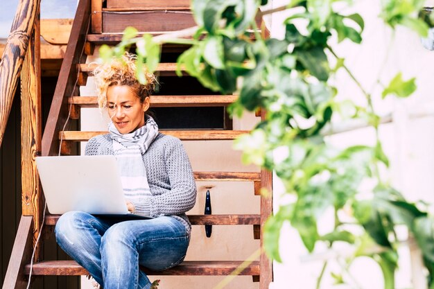 Bella giovane donna caucasica di mezza età che lavora al computer portatile connesso a internet all'aperto casa sedersi su una scala di legno