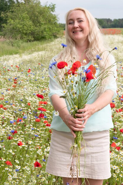 Foto una bella donna bionda di mezza età si trova in mezzo a un campo di papaveri in fiore