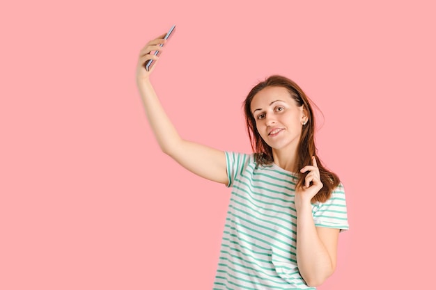 A beautiful middle-aged brunette takes a selfie posing on a pink background