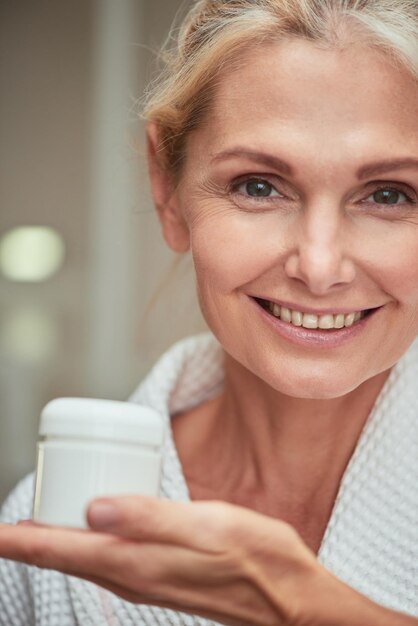 Beautiful middle aged caucasian woman holding cream bottle