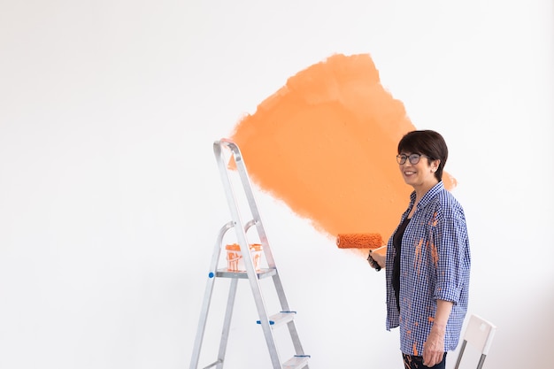 Beautiful middle-aged female painting the wall with paint roller. Portrait of a young beautiful