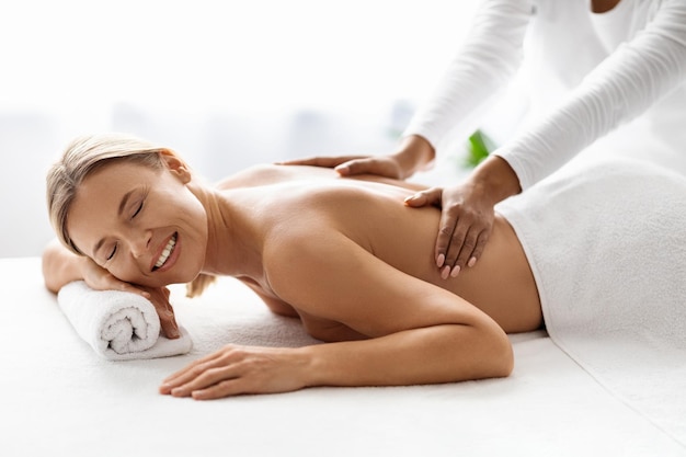 Beautiful middle aged lady receiving relaxing back massage from professional therapist