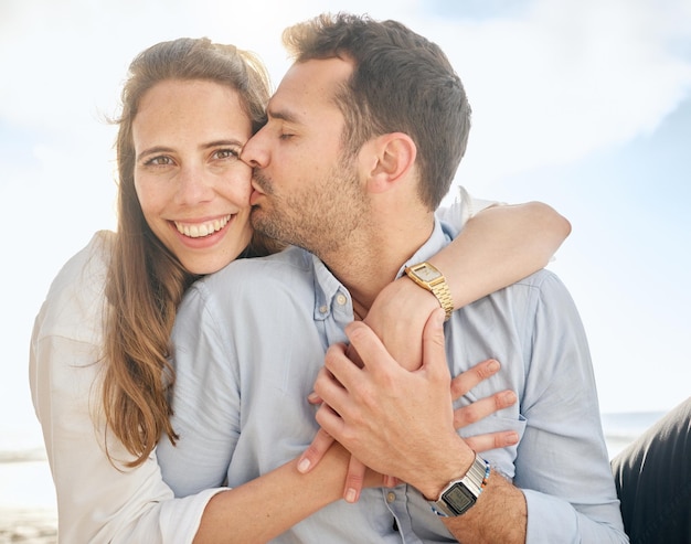 Beautiful middle aged woman being kissed on the cheek by her husband while sitting outdoors on the beach Affectionate married couple hugging on a romantic date showing love to his wife outside