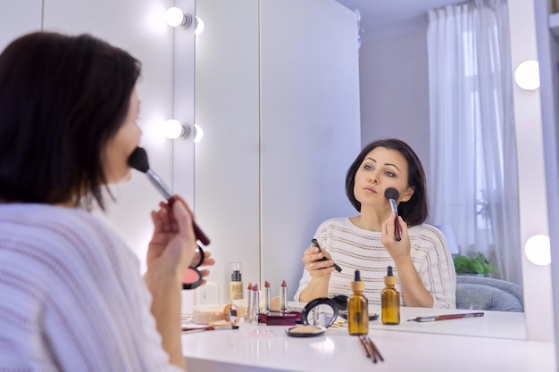 Beautiful middle aged woman doing makeup in front of a mirror