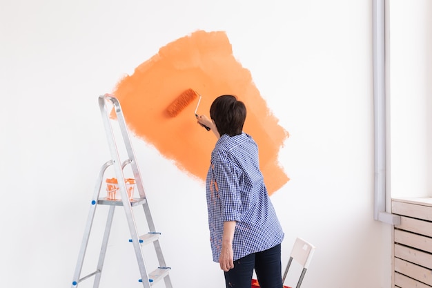 Beautiful middle-aged woman painting wall in her new apartment. Renovation and redecoration concept.