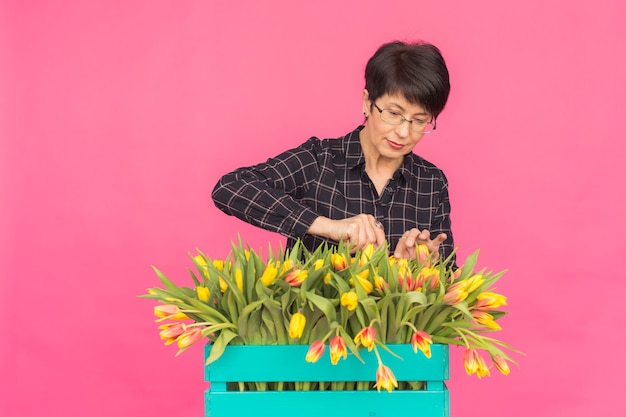 ピンクの背景に黄色のチューリップを持つ美しい中年女性。植物学、休日、ギフトのコンセプト