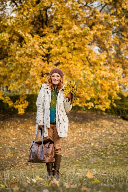 黄色い秋と通信する美しい中年女性革のバッグを持って自然の中を歩く幸せな女性