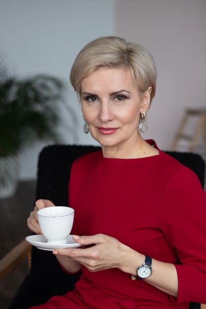 Beautiful middleaged woman in red dress sitting on a chair with a cup