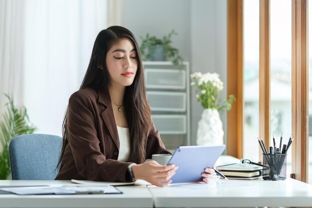 Beautiful millennial female entrepreneur sitting at workstation and reading email from client on digital tablet