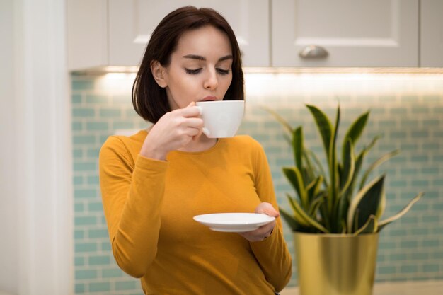 Beautiful millennial woman sipping hot tea kitchen interior