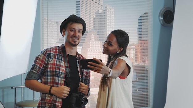 Beautiful model making selfie with handsome photographer in professional studio