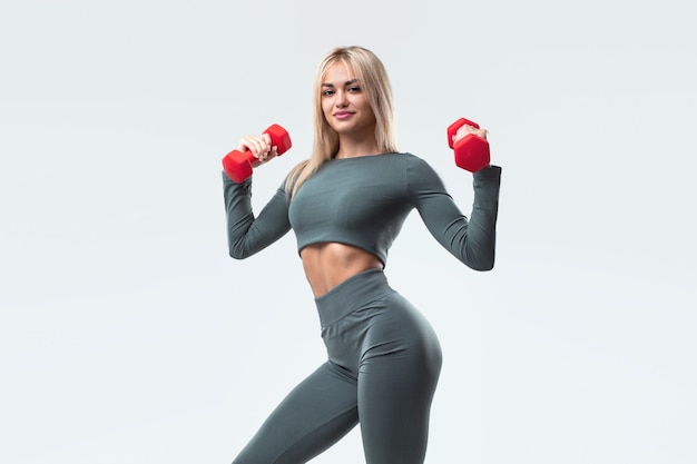 A beautiful model in sportswear with dumbbells on a white background