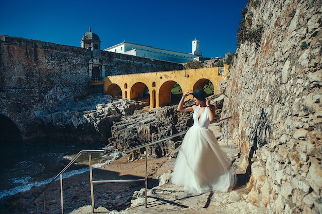 Beautiful model wearing white dress  is posing next to an old castle