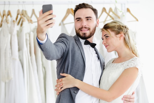 Beautiful model wedding couple holding smartphone online video call looking at screen