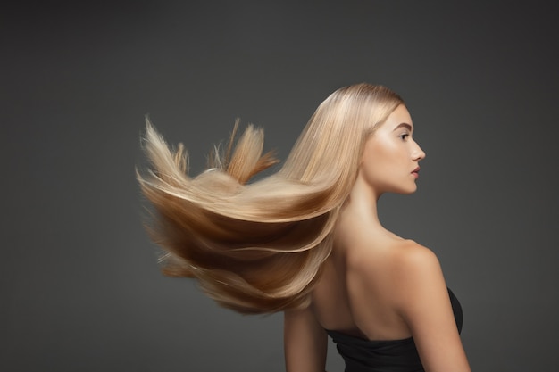 Beautiful model with long smooth, flying blonde hair isolated on dark grey studio wall