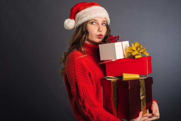 Una bellissima modella con un cappello di babbo natale e un maglione lavorato a maglia rosso tiene in mano molti doni.