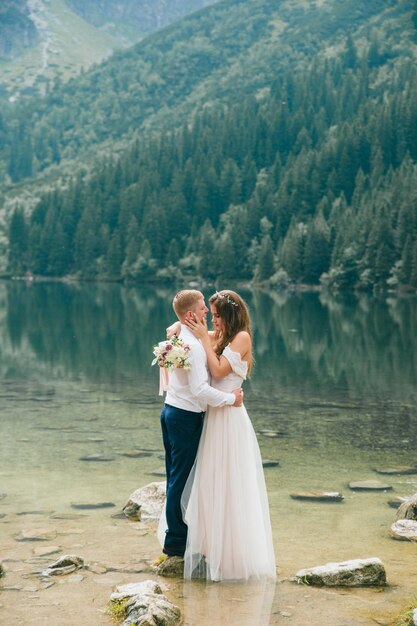 山の湖の近くの美しい現代のカップルは結婚式の写真を作る