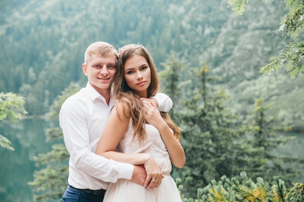 Belle coppie moderne vicino a un lago in montagna fanno foto di matrimonio