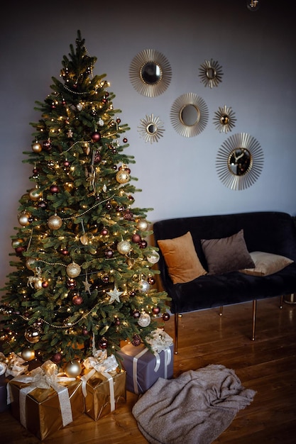 Beautiful modern gray apartment room decorated for New Year and Christmas Cute Christmas tree in a yellow garland and golden Christmas balls