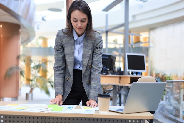 Beautiful modern woman is writing something down on paper documents while working in office.