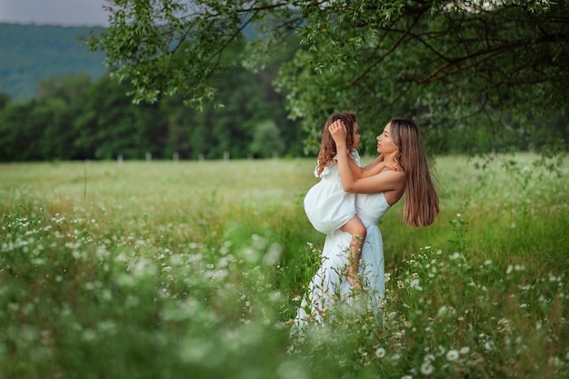 Красивая мама и ее маленькая дочь в белых платьях развлекаются на прогулке летом