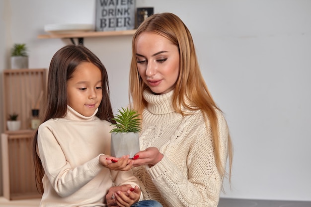 Beautiful mom and her small little daughter on weekend sitting on countertop consider a flower in a ...